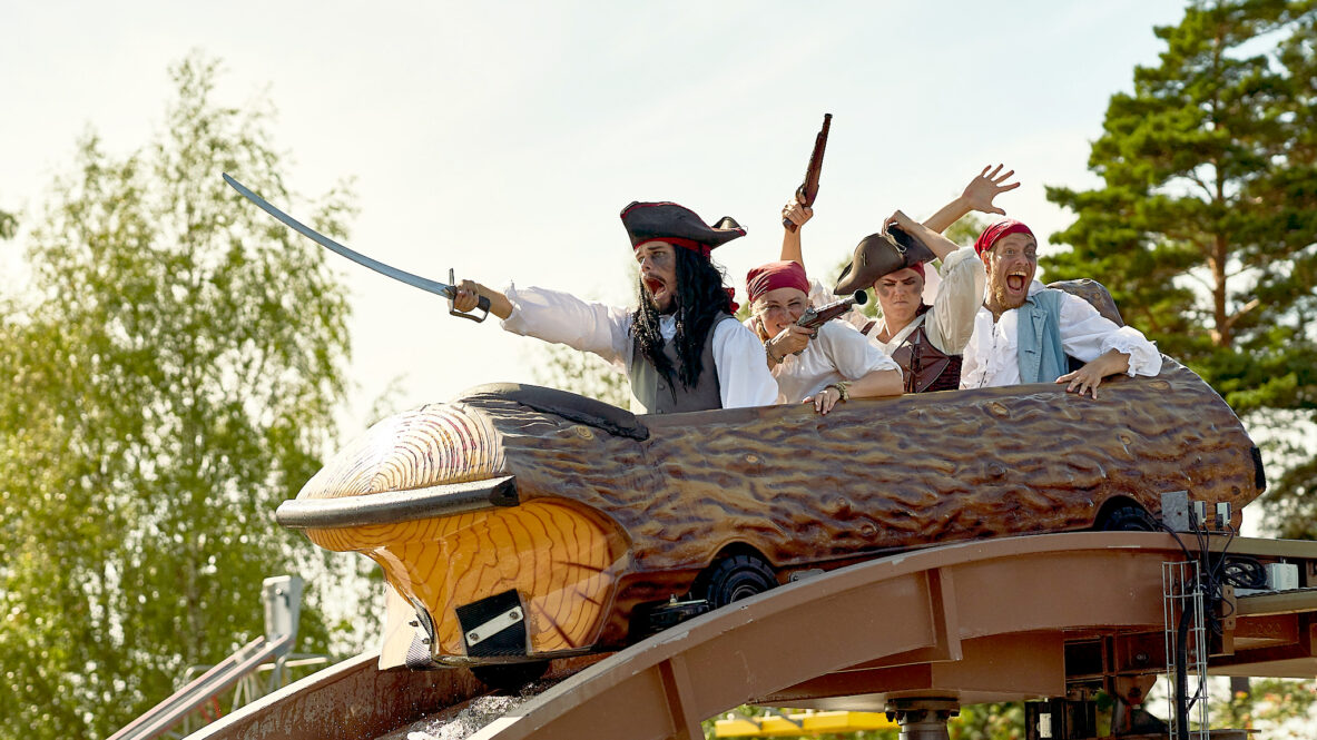 Fyra personer utklädda till pirater åker en stockbana i en nöjespark. De skriker och gestikulerar med svärd och pistoler i luften