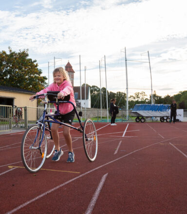 Ca 10-årig tjej med en racerunner-cykel på friidrottsbana utomhus