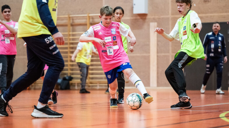 Kids playing indoor football. Wearing shirts in bright colours.