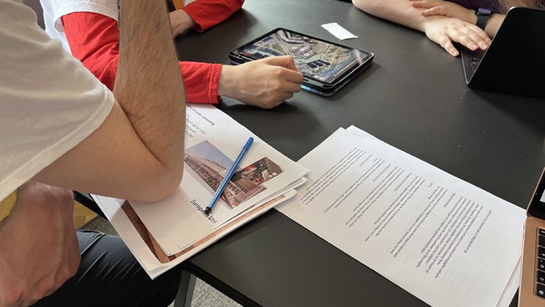 Armar och händer tillhörande tre personer som sitter runt ett bord och använder en iPad