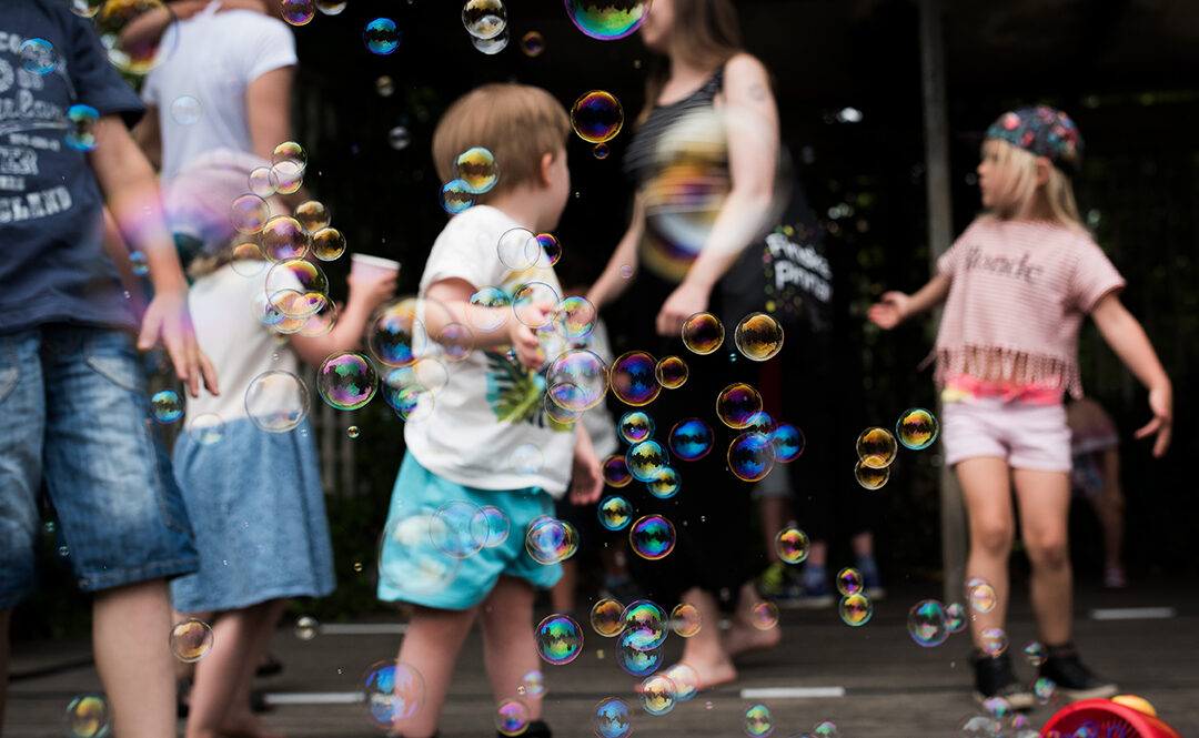 Barn och vuxna leker bland såpbubblor på en utomhusscen